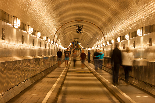 Old illuminated tunnel ( Elbtunnel) with sidewalks and road under River Elbe, blurred people, Hamburg, Germany.