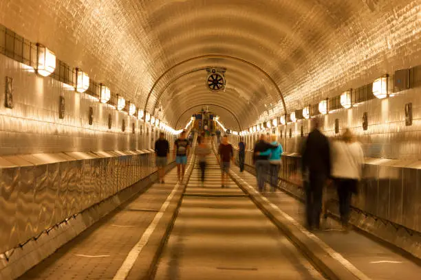 Old illuminated tunnel ( Elbtunnel) with sidewalks and road under River Elbe, blurred people, Hamburg, Germany.