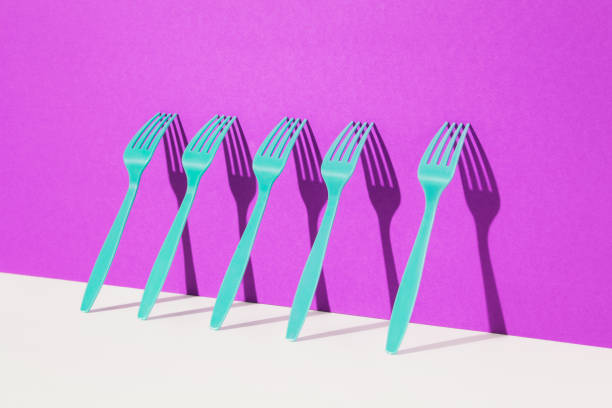 Close up of plastic blue forks in a row on two toned beige and pink background
