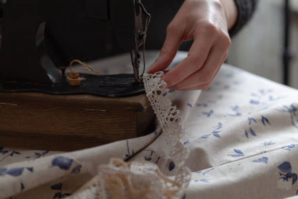 Handmade seamstress. Woman thin fingers hold the braid in a hand sewing machine close-up. Nearby lies a fabric with a blue pattern