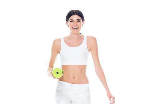 Waist up of aged 20-29 years old who is tall person with long hair caucasian female ready for yoga in front of white background wearing jogging pants who is cheerful and using exercise mat
