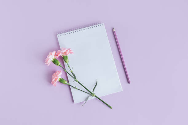 istock Notebook with blank page, pencil and Carnation flower on a violet pastel background. 1366111671