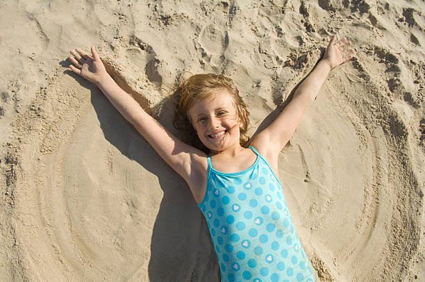 Angel in the sand Happy young girl, making angels in the sand. girls laying on beach stock pictures, royalty-free photos & images