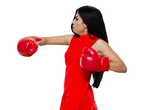 Waist up of aged 20-29 years old who is beautiful with black hair latin american and hispanic ethnicity young women standing in front of white background wearing glove who is showing cool attitude and boxing who is fighting