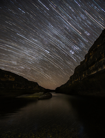 Stars stream across the clear night sky on the Pecos River in Texas. The reflections of the stars and the towering cliffsides give a sense of isolation and wonder.