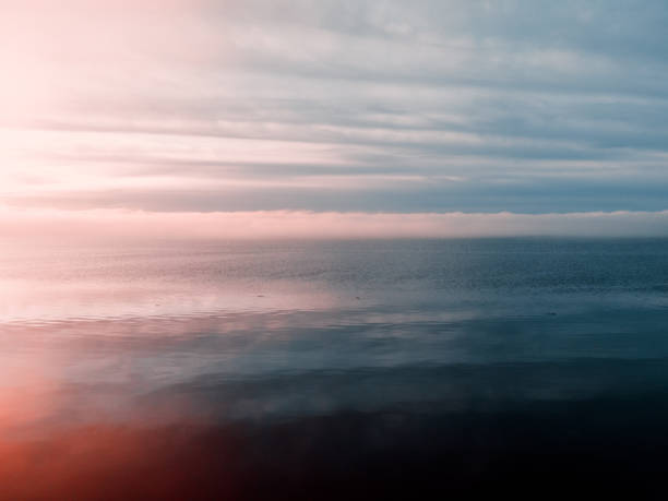 An epic setting sun cast pink and orange colors through foggy air and fluffy clouds in Washington state, over the saltwater of the Puget Sound.  Beauty in nature at it's finest.