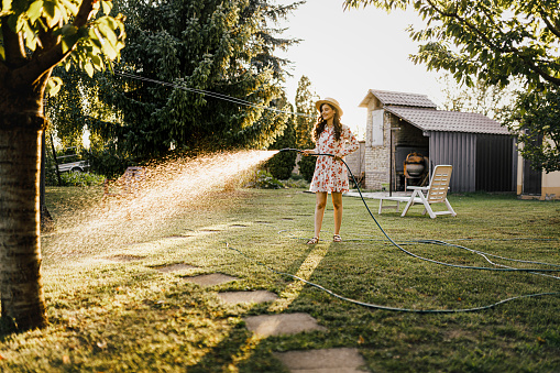 Shot of a woman watering plants with a garden hose in backyard