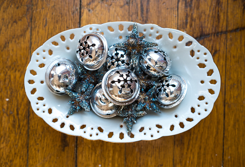 Silver Bells and Ornaments in a White Dish on a Wood Background