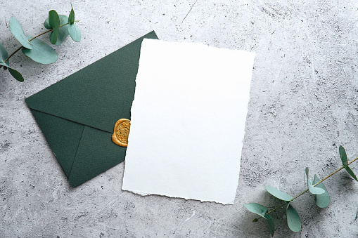Elegant wedding stationery set. Wedding invitation card template and green envelope on concrete background. Flat lay, top view, copy space.