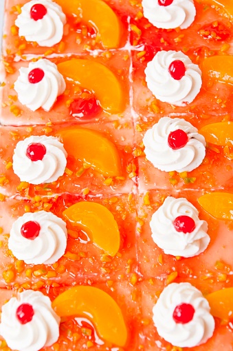 Freshly made yoghurt peach gateaux slices. The basis is a biscuit base, on top of which is a delicate layer of yoghurt, topped with aromatic peaches, covered with cake glaze, decorated with cream swirl and candied cherries, ensure heavenly - light cake enjoyment. This image is part of a series.