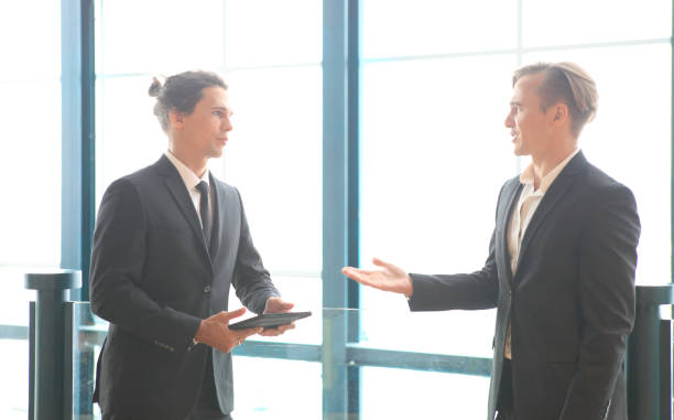 istock two young business people working and communicating while standing at the office with city building background. 1366138629