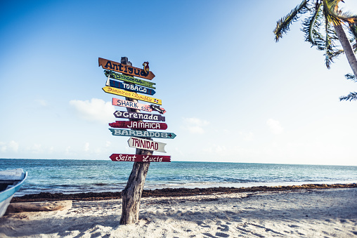 Multicolored sign showing many Caribbean travel destinations. There is one tourist walking in the background