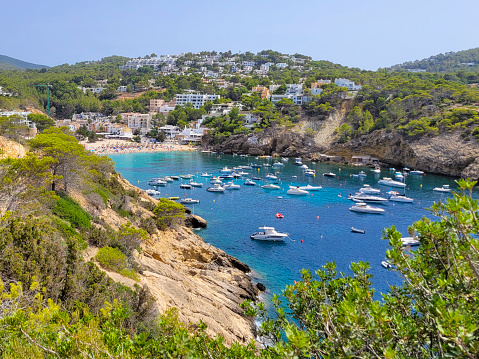 Rocky coastline, beach, cliffs of Ibiza, Spain in summer season.  Beautiful turquoise water of Mediterranean Sea. Sailboats and motor boats.