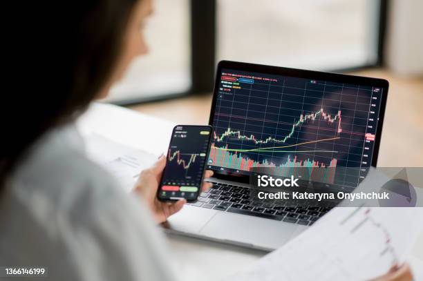 Successful Smart Woman Investor And Crypto Trader Using Laptop And Smartphone Analyzes Charts Of Trading In Stock Market And Digital Cryptocurrency Exchange Conducts Analysis Trading Crypto Coins Stock Photo - Download Image Now