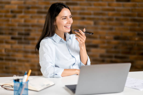 bella fiduciosa giovane adulta brunetta caucasica donna d'affari, agente, manager, siede in ufficio moderno parlando al telefono con i colleghi o un cliente in vivavoce, registra il messaggio audio - financial occupation audio foto e immagini stock