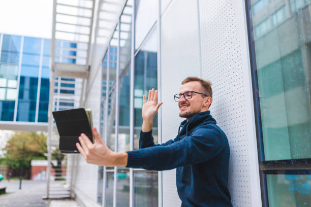 istock Young man with glasses talking in a video call on his tablet in an environment with modern architecture 1366149563
