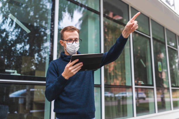 istock Young man with glasses looking for directions on his tablet while wearing a protective face mask outside an airport 1366150068