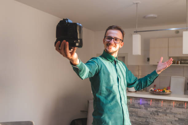 istock Young white male with glasses vlogging with a professional DSLR camera while explaining something 1366150812