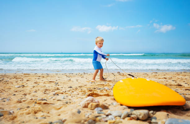 istock Little toddler pull surfboard to the sea waves 1366157977