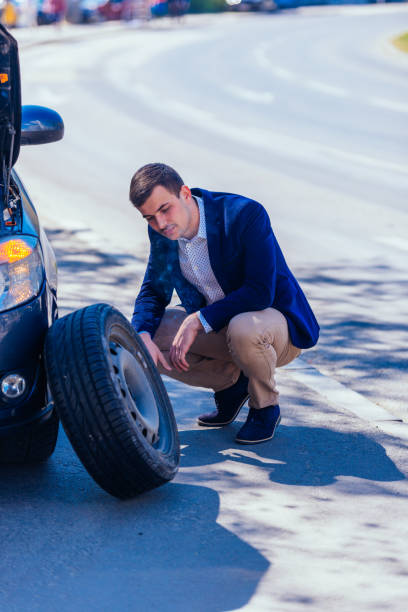 istock A formally dressed gentleman wearing a blue blazer is changing the flat tire on his car while being parked next to a busy boulevard. 1366161003