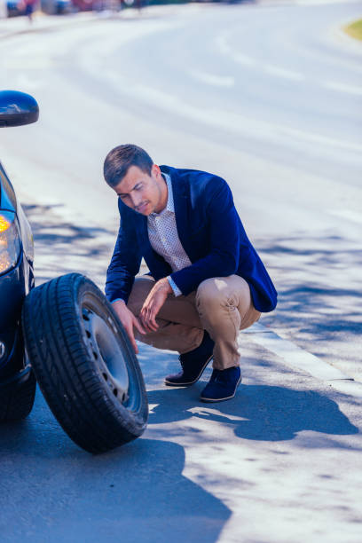 istock A formally dressed gentleman wearing a blue blazer is changing the flat tire on his car while being parked next to a busy boulevard. 1366161014