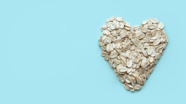 flocons secs de céréales à l’avoine. un flocon d’avoine avec une forme de cœur ou d’amour sur un fond pastel avec un espace de copie. - oatmeal oat heart shape rolled oats photos et images de collection