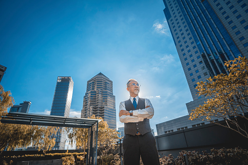 asian chinese company CEO arms crossed standing at rooftop of office building in city during morning looking away