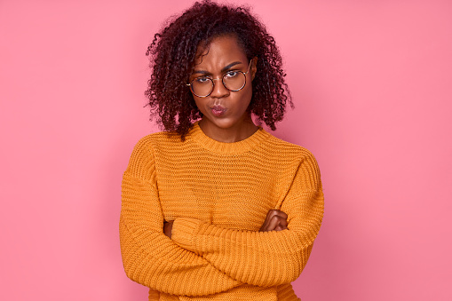 Sad angry young african american woman displeased looking at the camera with her arms crossed over a pink background in the studio. Concept of failure. Advertising space