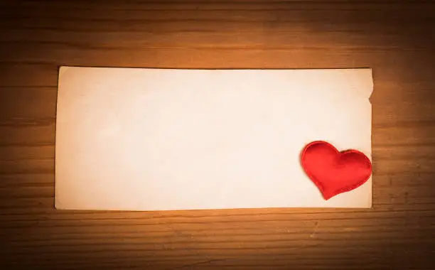 Old Blank Paper with a Red Heart on a Wooden Planks Background closeup