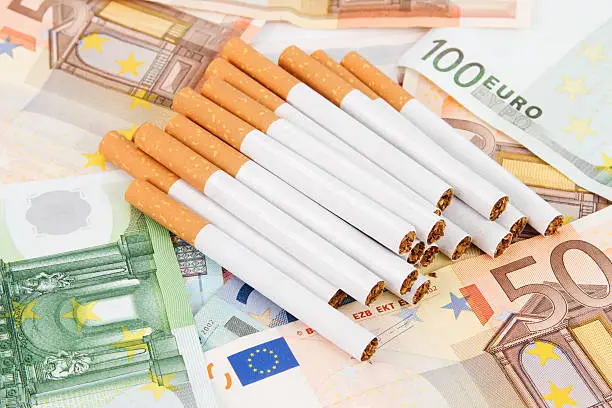 A lot of different Euro banknotes with a stack of cigarettes