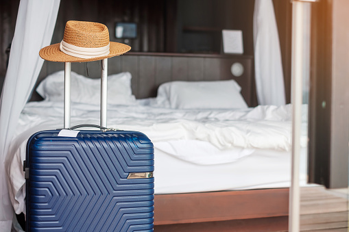 Blue Luggage with hat in modern hotel room after door opening. Time to travel, service, journey, trip, summer holiday and vacation concepts