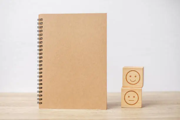 Photo of emotion face block and notebook on table. Emoticon for customer review, satisfaction, mood, mental health and feedback concept