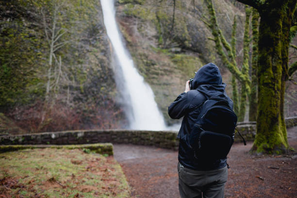 A photographer/videographer captures photos and video on his camera while exploring the waterfalls in the Columbia River Gorge of Oregon State.