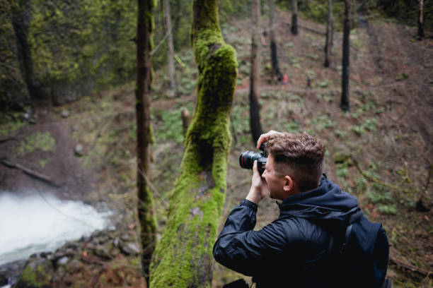 istock Photographer Using Camera To Take Photos of Waterfall in Oregon 1366190112