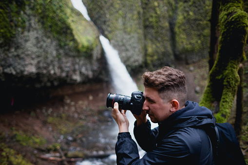 A photographer/videographer captures photos and video on his camera while exploring the waterfalls in the Columbia River Gorge of Oregon State.
