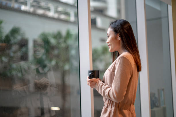 istock An asian  female having coffee while looking outside the window in office lounge area 1366190855