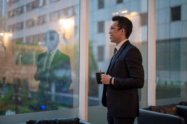 istock An asian male having coffee while looking outside the window in office lounge area 1366190870