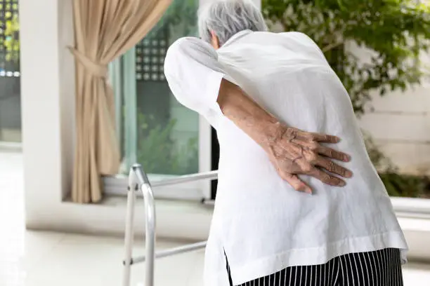 Photo of Hand of asian old elderly touch lower back muscles,senior patient with walker stick,suffering from back pain,backache from spinal joint problems,myositis,painful of lumbago,health care,medical concept