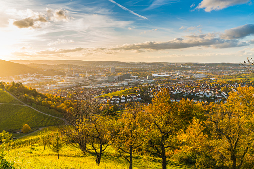 Germany, Stuttgart city panorama landscape view above industry houses, streets, stadium and highway at sunset in warm orange light