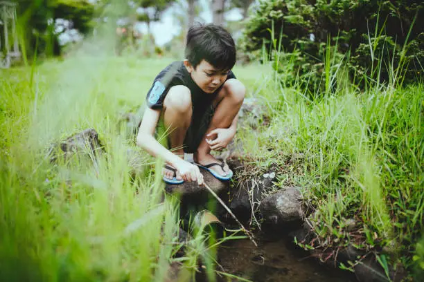 Photo of asian kid playing alone at the ditch at the yard