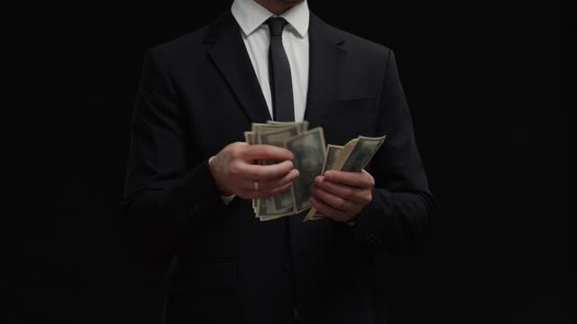 Unrecognized incognito man financial adviser holding and counts money banknotes wear black suit. Management shady business. Shadow Investor counting profit of dollar bills cash