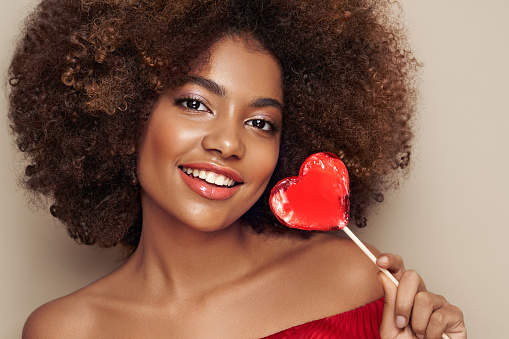 Beautiful portrait of an African girl with a heart shaped lollipop. Valentine's Day. Symbol of love