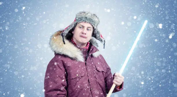 Photo of Man in winter clothes with a wooden light stick in his hands on a blue background with falling snow.
