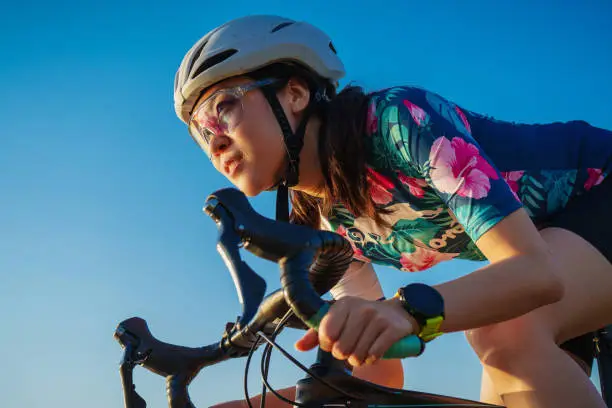 Photo of close up asian woman with athletic body shape in protective helmet and glasses riding bicycle on blue sky