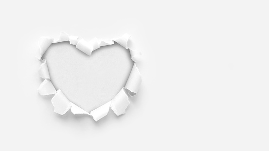 A paper hole with torn edges on a white background. Through paper. A ragged hole in the shape of a heart. Valentine's day. A symbol of love, romantic relationships. International Women's Day.