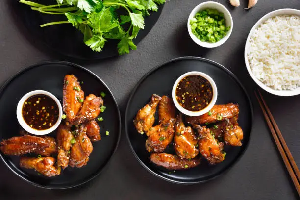 Sticky honey-soy chicken wings over dark stone background. Top view, flat lay
