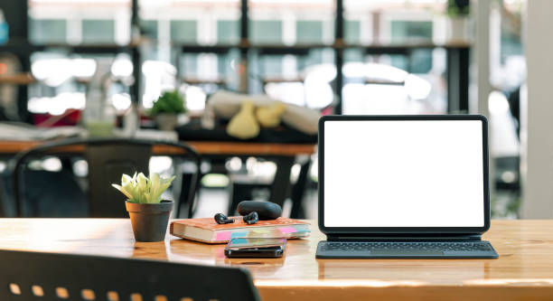 istock Mockup white screen portable tablet with magic keyboard on wooden table in co-workspace. 1366231710