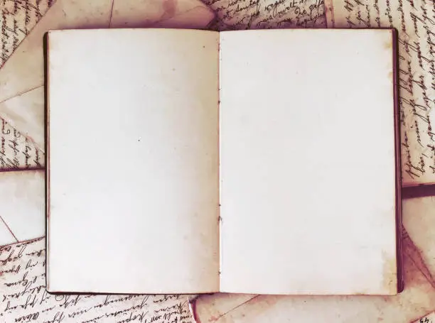 Overhead view of an open-wide journal on top of old scattered letters and papers from the beginning of the 20th century.