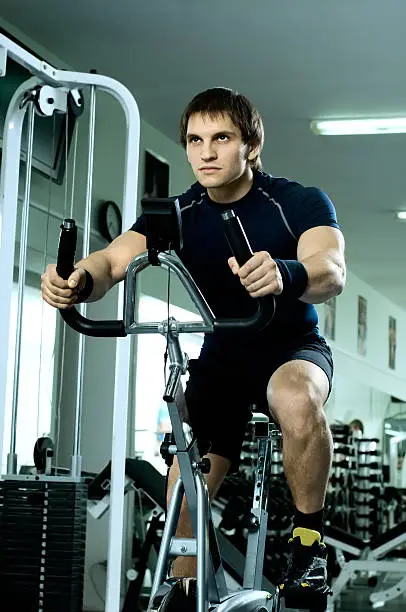 beautifull strong athletic guy,  execute exercise on exercise-bicycle, in  sport-hall