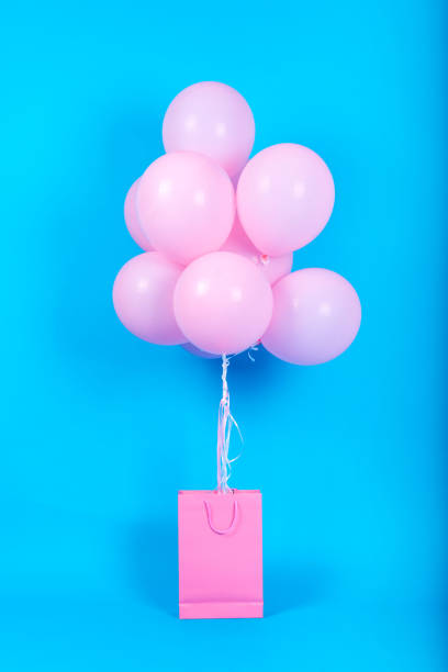 Pink birthday air balloons in blank pink shopping bag on blue background, copy space for text. Pink balloons in blank paper bag, free space. Valentine, birthday concept. Happy holiday flying balloons stock photo